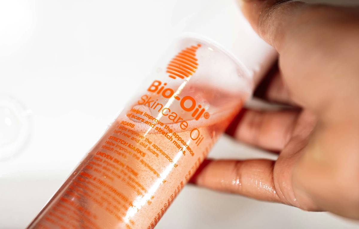 Woman applying moisturizing oil basic skin care routine to damp arms after shower