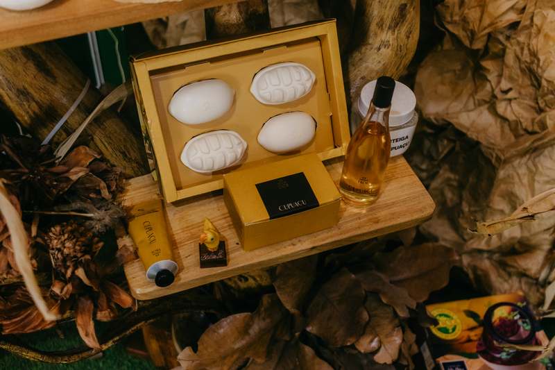 Minimalist flat lay of amber glass bottles filled with golden body oil, dried lavender, and a ceramic bowl with raw jojoba seeds on a linen cloth